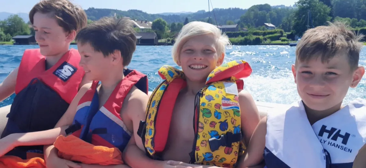 Kinder und eine Begleitperson mit Schwimmwesten auf einem Boot.